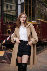 a lady in a white ruffle collared hirt, a pair of black shorts and a long trench coat
